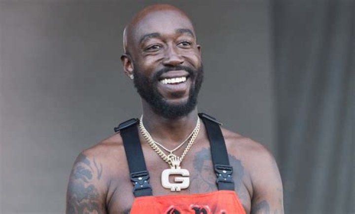Freddie Gibbs smiling at an event wearing a black shirt and chain.