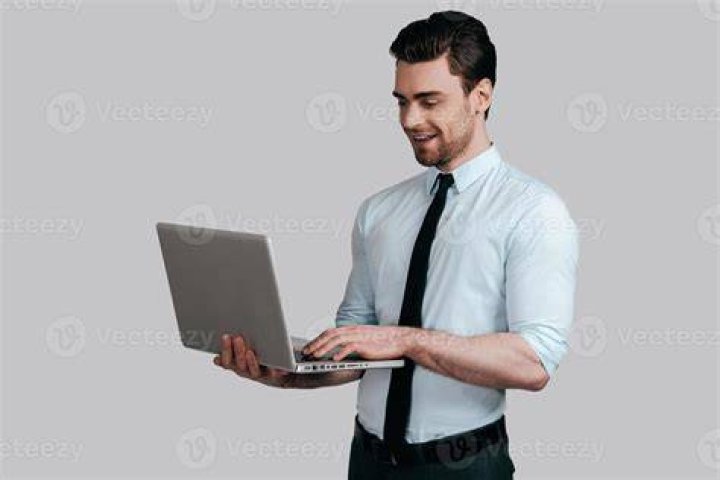man sitting at laptop holding a pencil and smiling